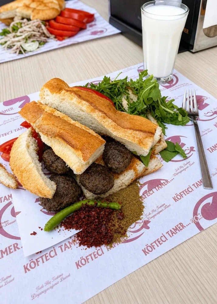Köfteci Tamer'in kâğıtta köfte servisi: köfte, ekmek, domates, baharat ve ayran